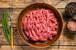 Raw mince lamb, ground mutton meat with herbs on a plate. Wooden background. Top view