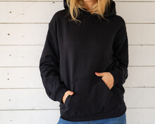 Sweatshirt Hoodie Mockup. Unrecognizable Woman Poses In A Black Sweatshirt Against The Background Of White Boards, Facing The Camera.