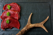 Raw Steak Meat From Roe Deer On The Bridlic  Chopping Board. Roe Deer Antler As A Decoration. Copy Space For Text.