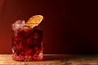 Glass with ice cocktail type americano or negroni with whole orange slice on red wall background and ray of light