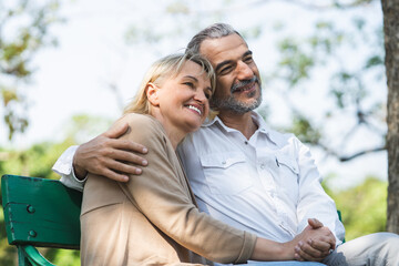 Elderly couple lifestyle concept. Husband embrace wife and sit on seat in the park relax on retirement life.