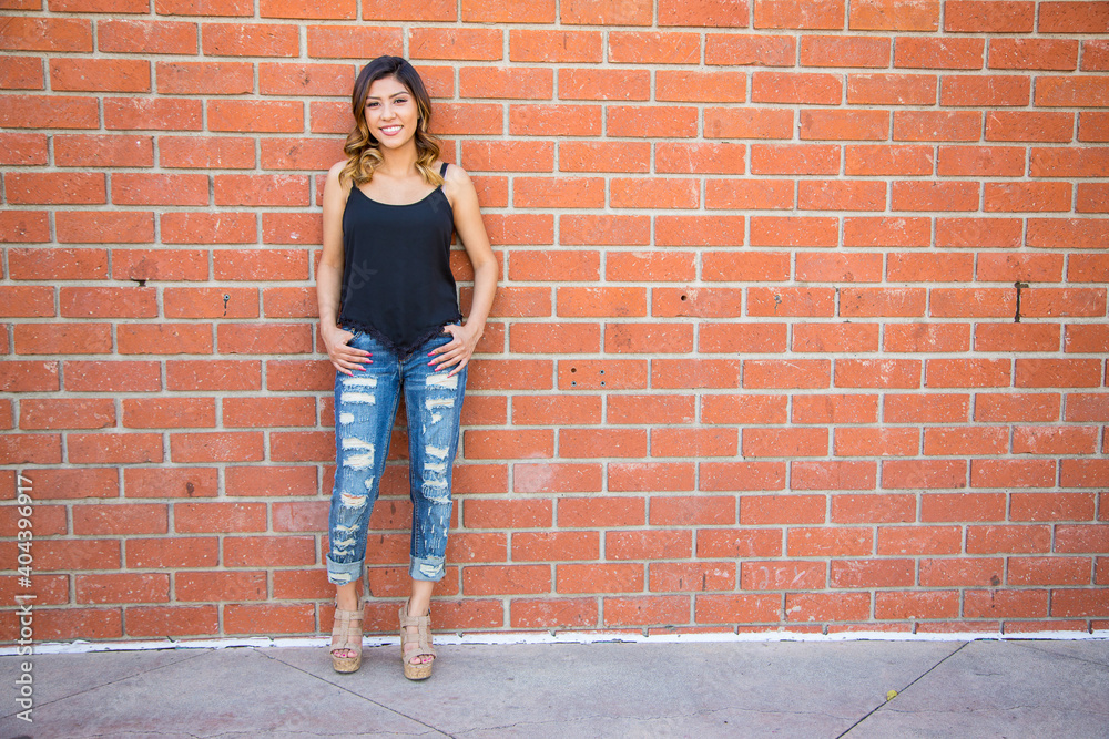 Hispanic young woman standing against a red brick wall wearing ripped ...