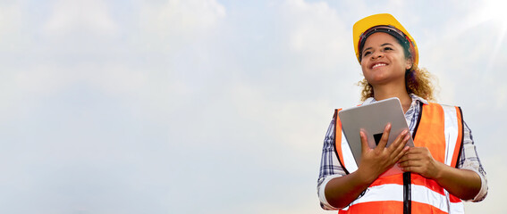 African American black female engineer or architect stands outdoors with tablet.