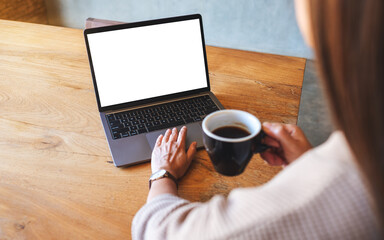 Mockup image of a woman using and touching on laptop touchpad with blank white desktop screen while drinking coffee