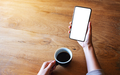 Top view mockup image of a woman holding mobile phone with blank white desktop screen while drinking coffee