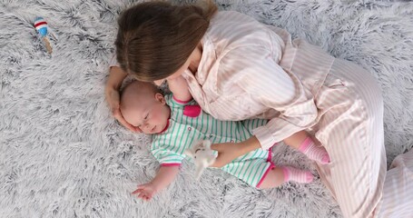 Sticker - Young woman playing with cute baby while lying on bed, top view