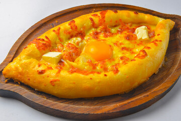 Khachapuri with cheese and egg on a wooden board over white background. Georgian cuisine concept.