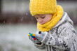 Beautiful blond toddler child, boy, with handmade knitted sweater playing in the park with first snow