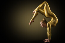 Flexible Woman Gymnast Doing Yoga Stretching Pose. Standing On Hands Back Bending. Gold Perfect Strong Healthy Acrobat Body. Over Black