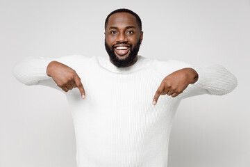 Wall Mural - Funny cheerful smiling young african american man 20s wearing casual basic sweater standing pointing index fingers down on mock up copy space isolated on white color wall background studio portrait.