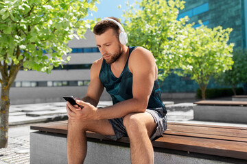 Poster - fitness, sport and technology concept - young athlete man with headphones and smartphone listening to music outdoors