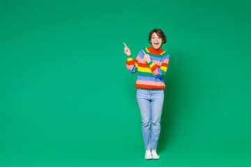 Wall Mural - Full length of excited shocked young brunette woman 20s years old wearing basic casual colorful sweater stand pointing index fingers aside up isolated on bright green color background studio portrait.