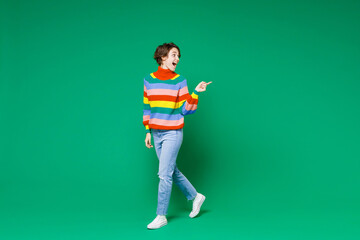 Wall Mural - Full length side view of excited shocked young brunette woman 20s in basic colorful sweater pointing index finger aside on mock up copy space isolated on bright green color background studio portrait.