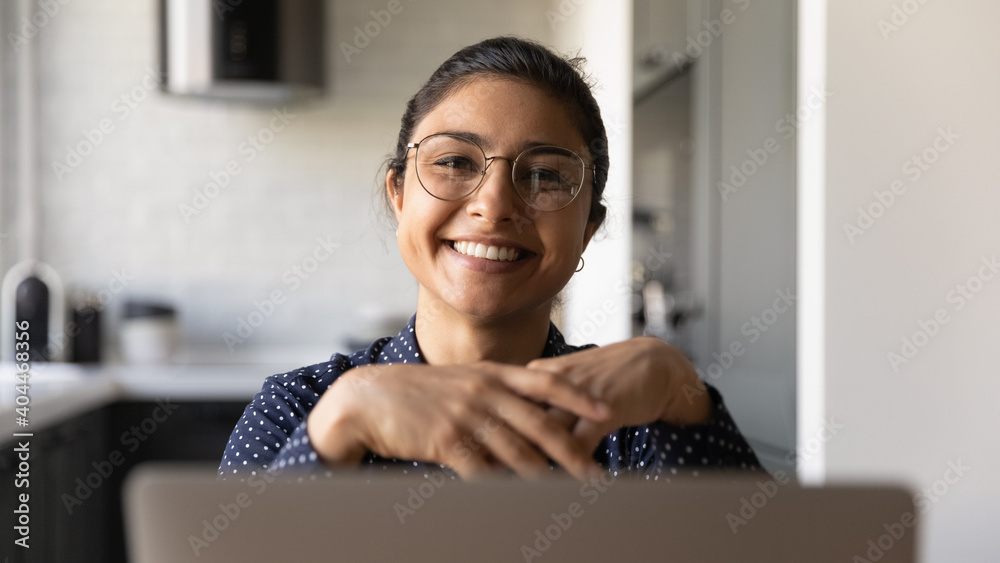 Close up view of smiling 20s young Indian woman in glasses working on laptop at home office. Happy millennial ethnic female wear spectacles for eyesight correction using computer at workplace. - obrazy, fototapety, plakaty 