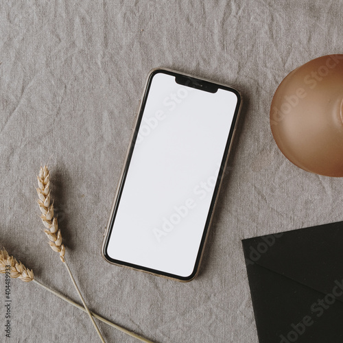 \Blank screen smart phone, decorations, ear / wheat ear stalks on grey washed linen cloth. Flat lay, top view minimalist lifestyle blog, website template. Copy space mockup.