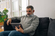 © cherryandbees - man sitting on sofa at his home and using digital tablet