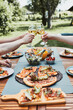 © Przemek Klos - Friends making toast during summer picnic outdoor dinner in a home garden. Close up of people holding wine glasses with white wine over table with pizza, salads and fruits. Dinner in a orchard