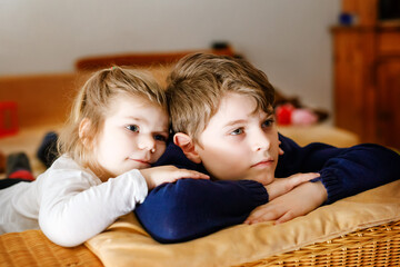 Cute little toddler girl and school kid boy watching animal movie or movie on tv. Happy healthy children, siblings during coronavirus quarantine staying at home. Brother and sister together.