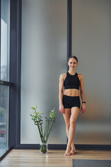 Standing and smiling. Young woman in sportive wear and with slim body have fitness yoga day indoors