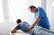 © LIGHTFIELD STUDIOS - middle aged chiropractor working with young and injured african american patient on massage table in clinic