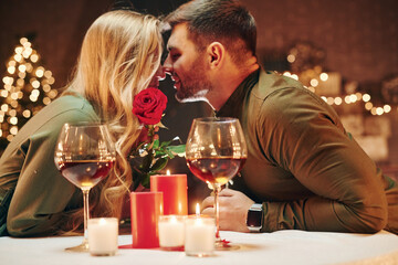 Holding beautiful red rose. Young lovely couple have romantic dinner indoors together