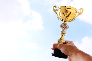 Wall Mural - Man holding up a trophy cup as a winner against the blue sky. Award and victory concept