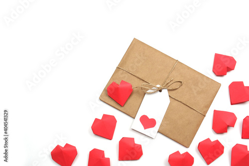 Gift wrapped in brown craft paper, tied with twine with a bow, with label with heart, surrounded by several handmade red 3D paper hearts on white background isolated copy space 