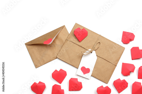Envelope from craft paper with red heart and gift wrapped in brown craft paper, tied with twine with a bow, with label with heart, surrounded by several handmade red 3D paper hearts white background 