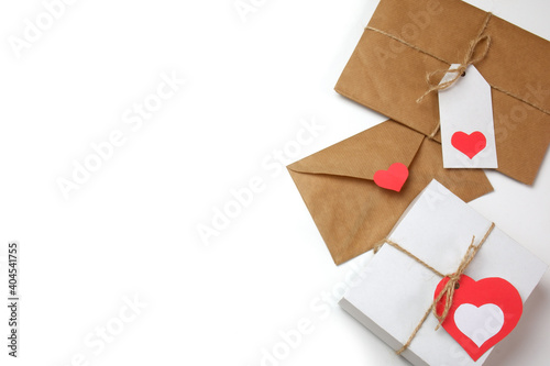 White gift box with red label in a heart form, gift wrapped in brown craft paper, tied with twine with a bow, envelope from craft paper with red heart on white background isolated 