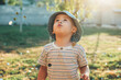 © Strelciuc - Caucasian boy is looking up at the blown confetti wearing a blue hat in a sunny summer day in the garden