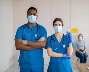 Poster - Portrait of doctors in medical masks and uniforms holding syringe with covid-19 vaccine at health centre