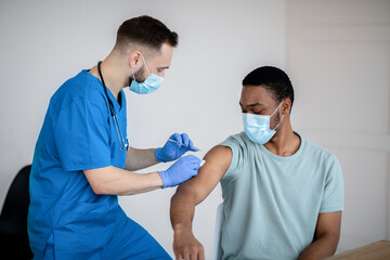 Poster - Doctor in face mask giving covid-19 vaccine injection to black male patient during vaccination campaign at clinic