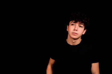 Attractive young man with curly hair posing on black studio background