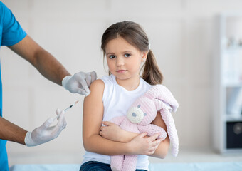 Poster - Lovely little girl with toy rabbit receiving covid-19 vaccine injection at clinic. Immunization against global virus