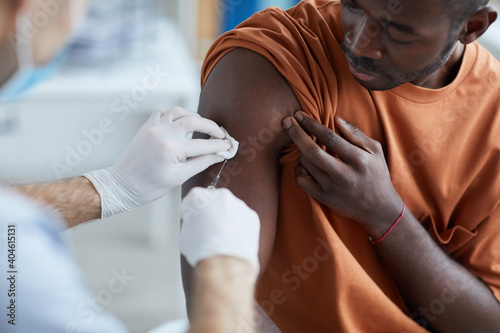 Obraz Dibond Close up of unrecognizable male nurse injecting vaccine in shoulder of African-American man during covid vaccination in clinic or hospital, copy space
