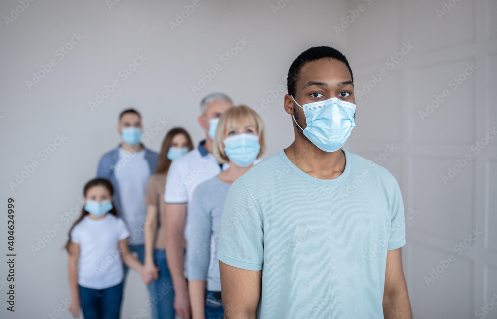 Young black guy in protective mask standing in line at hospital, waiting for vaccination against coronavirus, free space - obrazy, fototapety, plakaty 