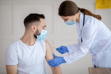 Poster - Vaccination against covid-19. Female doctor injecting coronavirus vaccine to male patient's arm at health centre