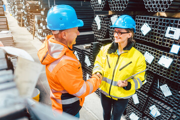 Customer and worker in steel delivery warehouse shaking hands