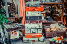 Racked Suitcases In Front Of Antique Shop. Colorful Old Suitcases. Old Plaques And Books