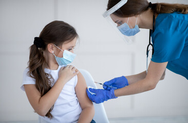Poster - Covid-19 vaccination. Little girl in protective mask receiving coronavirus vaccine injection from doctor at clinic