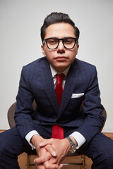 A young Latino businessman sitting in a dark blue suit and tie on a white background