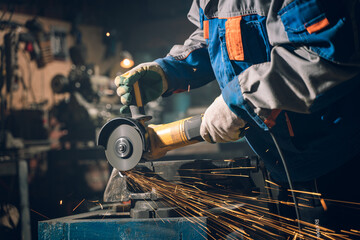 Wall Mural - Locksmith in special clothes and goggles works in production. Metal processing with angle grinder. Sparks in metalworking