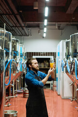 Sticker - Young brewer in workwear looking at glass of beer in his hand after preparation