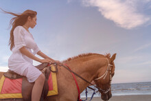 Side View Of Woman Horseback Riding At Beach Against Sky