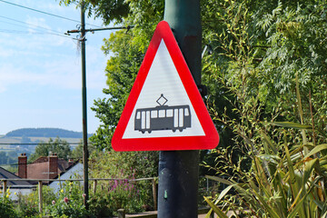 A red and white triangular warning sign of a tram crossing at Colyton station in Devon