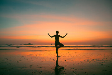 Wall Mural - An woman practicing yoga on the ocean side, the silhouette of awesome sunset.