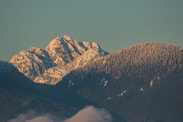 Wall Mural - the snow-covered mountain range surrounded by heavy white cloud  with orange sunlight hitting on the peak near sunset