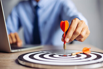 Wall Mural - Businessman holding a darts aiming at the target center business goal concept - business targeting, aiming, focus concept,metaphor to target marketing or target arrow to business successconcept.