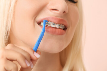 Young woman with dental braces and toothbrush on color background