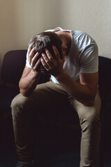 A young man in a state of crisis and despair. The white guy is sitting on a chair and holding his head with his hands. Stalemate or male impotence